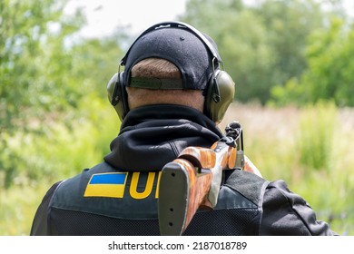 Portrait Of A Male Shooter 30-35 Years Old With A Sports Rifle On His Shoulder, Wearing Glasses And Tactical Headphones For Shooting Against The Background Of Nature.