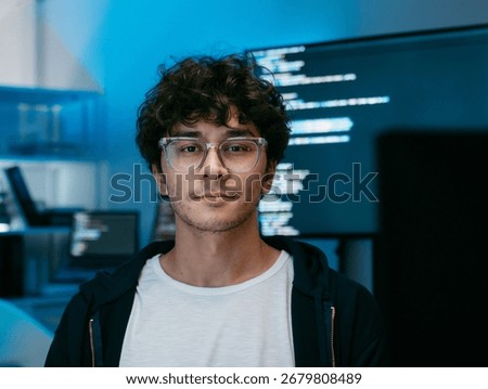 Portrait of Male software developer, Computer programmer looking at camera sits at desk in software and tech company office. Confident Smile Programmer working in Creative office at night.