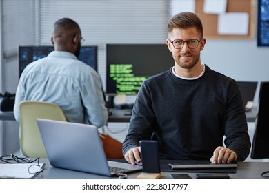 Portrait of male software developer smiling at camera while sitting at workplace in office, copy space