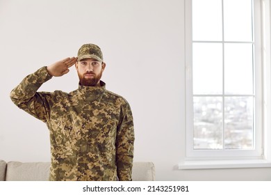 Portrait of male soldier in uniform saluting located indoors at home. Man US officer in military camouflage make hand gesture show respect. Army greeting sign. - Powered by Shutterstock