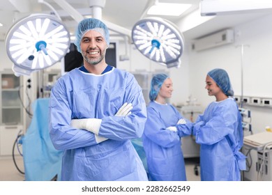 Portrait of male surgeon standing with arms crossed in operation theater at hospital. Team surgeons are performing an operation, middle aged doctor is looking at camera, in a modern operating room - Powered by Shutterstock