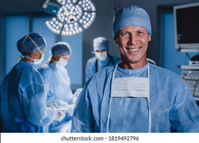 Portrait of male surgeon with team of doctors on background in operation room.
