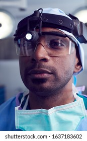 Portrait Of Male Surgeon Wearing Protective Glasses And Head Light In Hospital Operating Theater