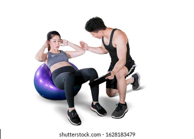 Portrait Of Male Trainer Helping Young Woman Doing Workout With Pilates Ball, Isolated On White Background