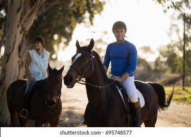 Portrait Of Male Trainer With Woman Riding Horse At Barn