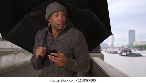 Portrait Of  Male With Umbrella Putting Phone Away On Nippy Day In England