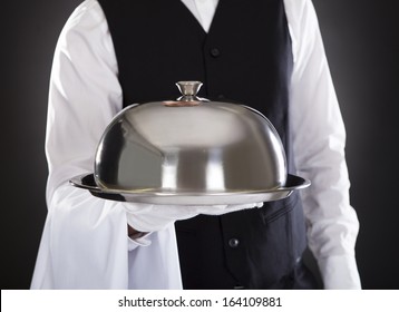 Portrait Of A Male Waiter Holding Tray And Lid Over Black Background