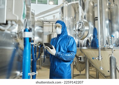 Portrait of male worker in protective suit operating equipment at factory and using digital tablet, copy space - Powered by Shutterstock