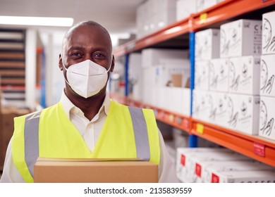 Portrait Of Male Worker Wearing PPE Face Mask Holding Box Inside Warehouse