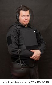 Portrait Of A Man 25-30 Years Old In A Bulletproof Vest And Tactical Headphones For Shooting On A Black Background.