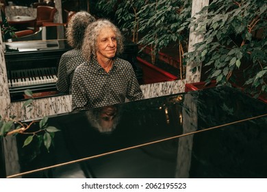Portrait of man, age 60 - 65 years old, gray curly hair, sitting at piano and playing piece of music, focused, injoing melody. 