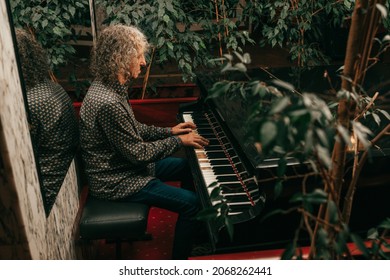 Portrait of man, age 60 - 65 years old, gray curly hair, sitting at piano and playing piece of music, focused, side view. 