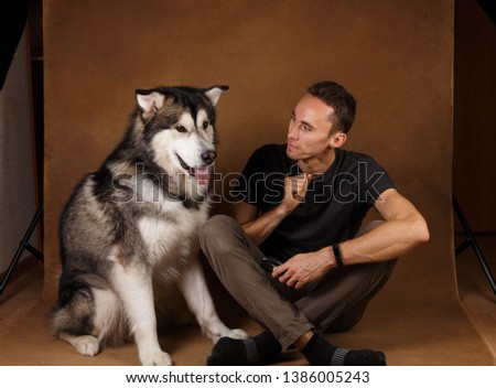 Portrait of a man and alaskan malamute dog stitting on brown blackground. Man training dog. Communication dog and owner