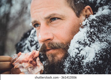 Portrait of a man with a beard devouring raw meat. Hungry northern bearded eats meat. Survivor northern bearded man with a piece of meat. 