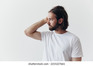 Portrait Of A Man With A Black Thick Beard And Long Hair In A White T-shirt On A White Isolated Background Emotion Of Sadness And Longing