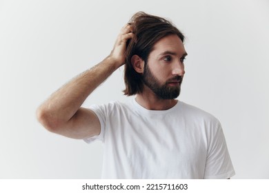 Portrait Of A Man With A Black Thick Beard And Long Hair In A White T-shirt On A White Isolated Background Emotion Of Sadness And Longing