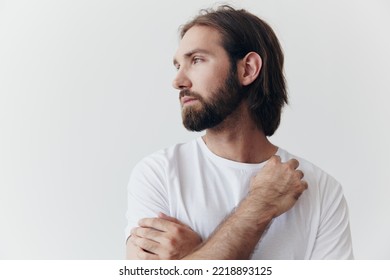 Portrait Of A Man With A Black Thick Beard And Long Hair In A White T-shirt On A White Isolated Background Emotion Of Sadness And Longing