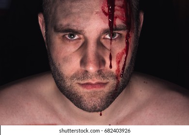 Portrait of man with blood on his face on dark background.