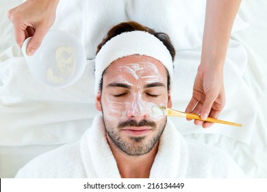 Portrait of man with clay facial mask in beauty spa. 