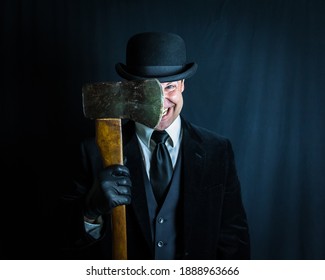 Portrait of Man in Dark Suit and Bowler Hat Holding Axe Blade Next to His Face on Black Background. Concept of Horror Movie Murderer. Maniacal Grin and Violent Insanity.