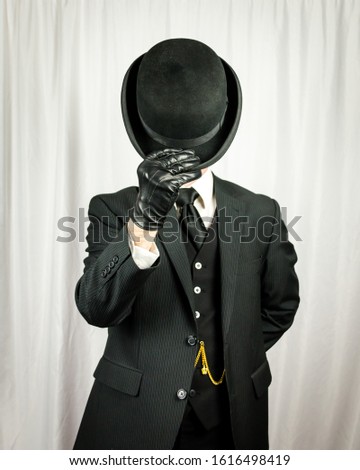 Portrait of Man in Dark Suit and Leather Gloves Doffing Bowler Hat. Concept of Classic and Eccentric English Gentleman. Polite British Butler.