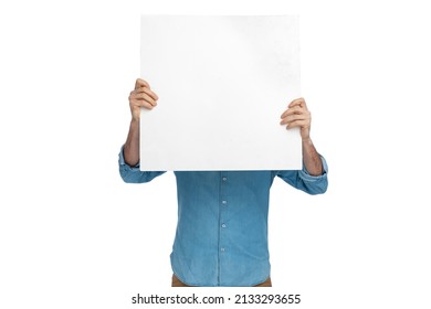 portrait of man in denim shirt covering face with white empty board in front of white background in studio