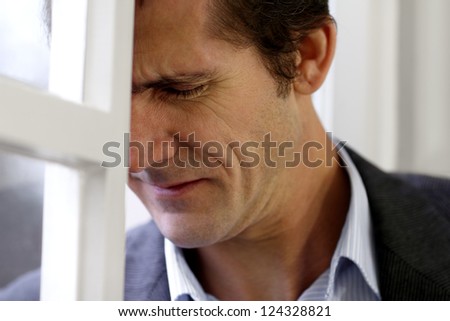 Portrait of a man in despair, misery or sorrow leaning against a window