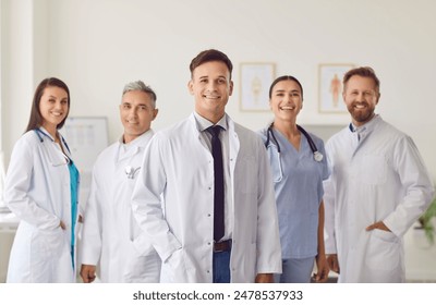 Portrait of a man doctor standing with a team of other doctors and nurses in the hospital. Group portrait highlights the clinic medical staff, showcasing teamwork and dedication to healthcare.