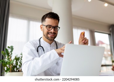 Portrait Of Man Doctor Talking To Online Patient On Laptop Screen Sitting At Clinic Office Desk Giving Online Consultation For Domestic Health Treatment. Telemedicine Remote Medical Appointment