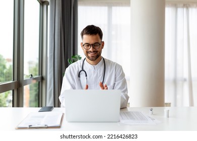 Portrait Of Man Doctor Talking To Online Patient On Laptop Screen Sitting At Clinic Office Desk Giving Online Consultation For Domestic Health Treatment. Telemedicine Remote Medical Appointment