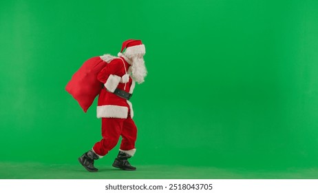 Portrait of man dressed as Santa on chroma key green screen background. Santa Claus in red outfit carrying bag of gifts and walking. Side view. - Powered by Shutterstock