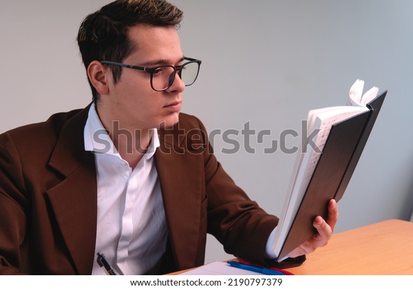 Portrait of a man dressed in a suit reading.\
Business man on a white background. Blond man reading the notes in\
his notebook. Blond boy dressed in brown suit, shirt and glasses.\
High quality photo