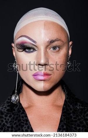 portrait of man with earrings and spectacular makeup on half face isolated on black