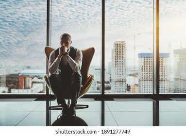 A portrait of a man entrepreneur in a state of worry and dismay sitting on an armchair in front of the window of a luxury office high-rise and thinking about how to solve recent business issues - Shutterstock ID 1891277749