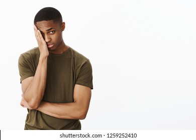 Portrait of man feeling embarrassed making facepalm gesture putting hand to half of face peeking at camera with tired blushing expression standing displeased and exhausted over gray background