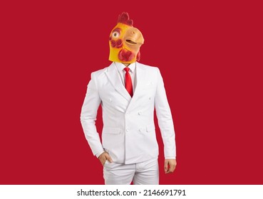 Portrait of man in funny disguise. Happy proud rich young businessman wearing elegant white suit and silly freaky yellow masquerade chicken mask posing against red studio background