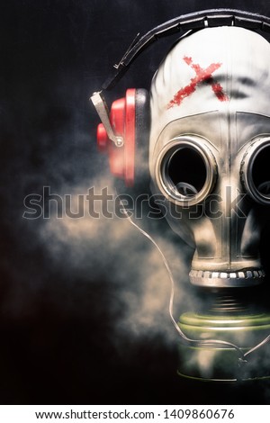 Portrait of a man in a gas mask and with headphones. Smokescreen. Music lover listening to music. Marked. The cross on the mask.