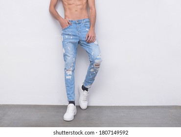 Portrait of man, half naked, showing strong body, wearing black torn jeans on gray background

