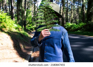 Portrait Of A Man With A Hat And Texan Clothes Covering His Face With A Fern Leaf. Fashion Concept