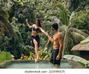 Portrait of man helping girlfriend entering the pool at resort. Loving couple in swimming pool. - Powered by Shutterstock