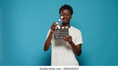 Portrait Of Man Holding Clapperboard To Cut Scenes In Movie Industry. Cheerful Person Using Chalkboard For Film Making Production And Cinematography In Studio. Young Adult With Clap Board