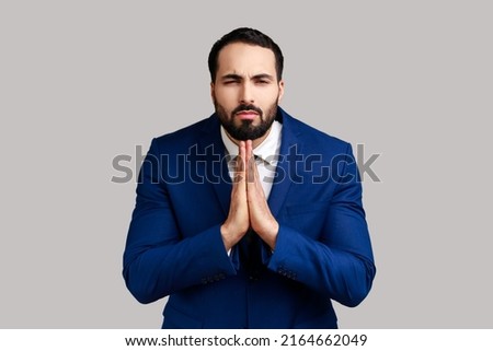 Portrait of man holding hands in prayer, looking with imploring pleading expression, begging help, asking forgiveness, wearing official style suit. Indoor studio shot isolated on gray background. Foto stock © 