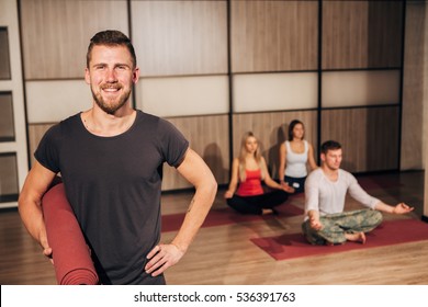 Portrait of a man holding yoga mat and smiling with his hand behind head