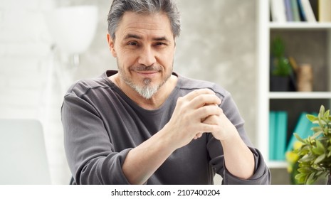 Portrait Of Man At Home Sitting At Desk, Working, Looking At Camera. Happy Smile, Grey Hair, Beard. Portrait Of Mature Age, Middle Age, Mid Adult Man In 50s.