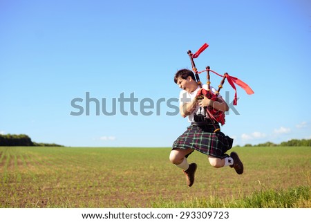 Portrait of man jumping high with pipes in Scottish traditional kilt on green outdoors copy space summer field
