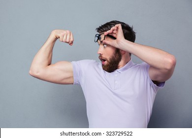 Portrait of a man looking at his biceps with delight over gray background - Powered by Shutterstock