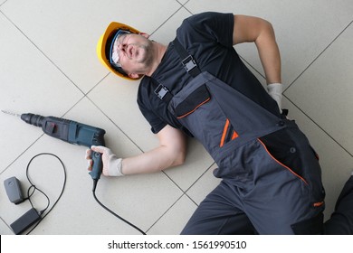 Portrait Of Man Lying At Floor With Drill In Hands. Handyman Fell Off Ladder Holding Back. Incident At Work. Dangerous Profession Of Person With Backache And Pains In Spine