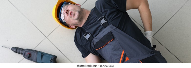 Portrait Of Man Lying At Floor With Drill In Hands. Handyman Fell Off Ladder Holding Back. Incident At Work. Dangerous Profession Of Person With Backache And Pains In Spine