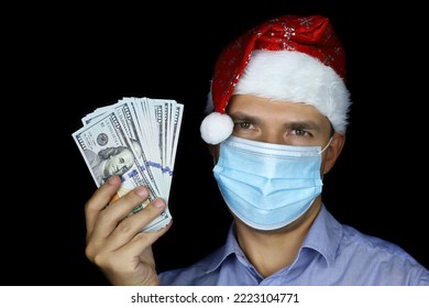 Portrait of man in mask and Santa hat with US dollars in hand on black background. Bonus gift for Christmas celebration, New Year holiday during coronavirus pandemic