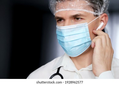 Portrait Of Man In Medical Mask With Wireless Earphone In The Ear. Doctor With Headset, Voice Call And Advice Concept